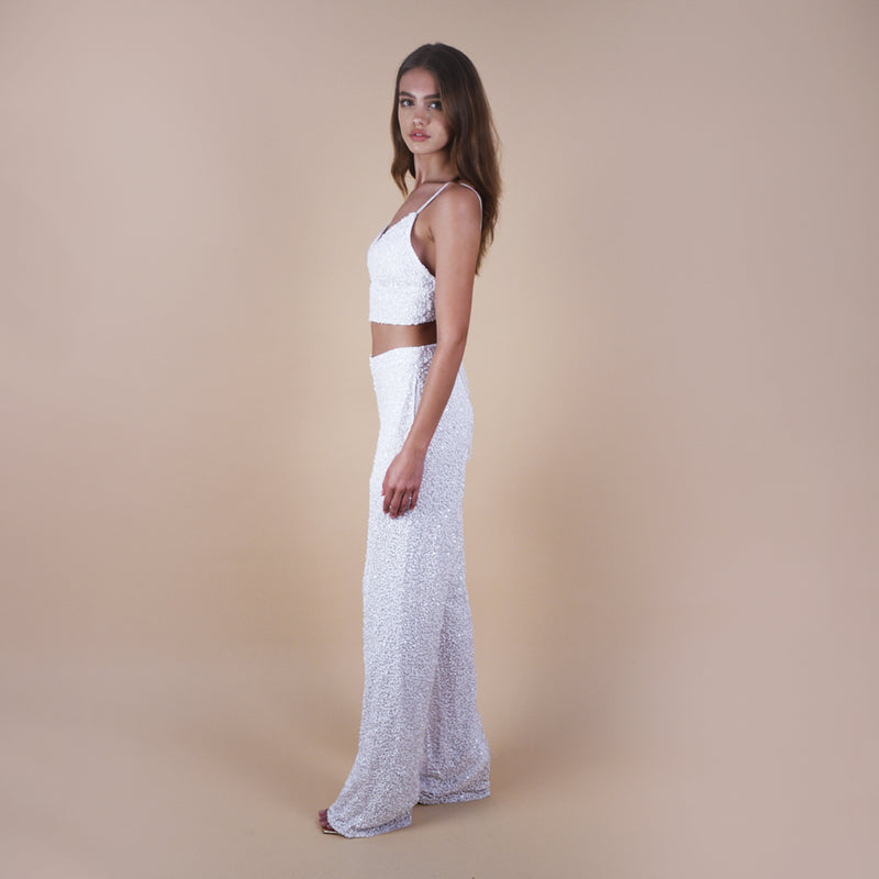 off-white Anastasia Beaded Bralette Crop Top. Handcrafted with intricate beadwork, this versatile party outfit features a lace-up tie closure at the back, ensuring a perfect fit. Stand out at events with this chic and stylish crop top. Side View in sequin pants