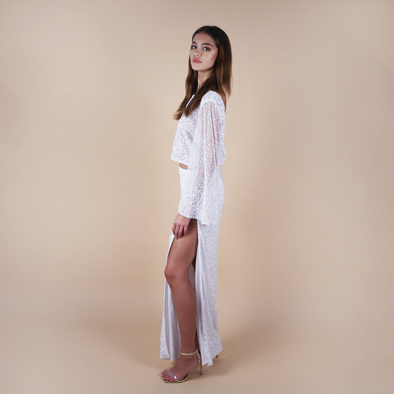 Giselle Off-White Sequin Maxi Long Skirt. Perfect for a boho look, nights out, weddings, brides, white parties and spring transitions. Handcrafted with intricate sequin embellishments, this skirt adds glamour to any occasion. Indulge midi skirts, high waisted skirt, skirt with a slit, long skirt. Showing the side view on the slit