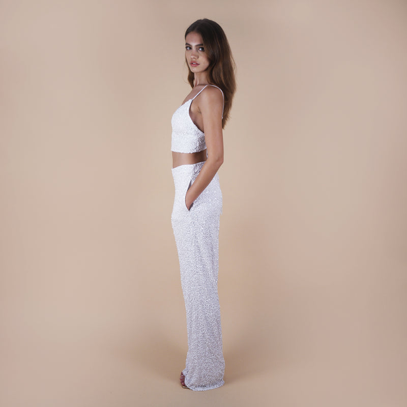 off-white Anastasia Beaded Bralette Crop Top. Handcrafted with intricate beadwork, this versatile party outfit features a lace-up tie closure at the back, ensuring a perfect fit. Stand out at events with this chic and stylish crop top. Side view with sequin pants.