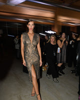 Model in a sparkly dress walking on a runway with an audience in the background.
